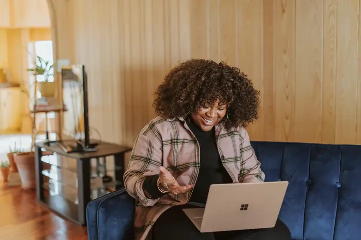 Mujer afroamericana profesional interactuando con su laptop en un sillón.